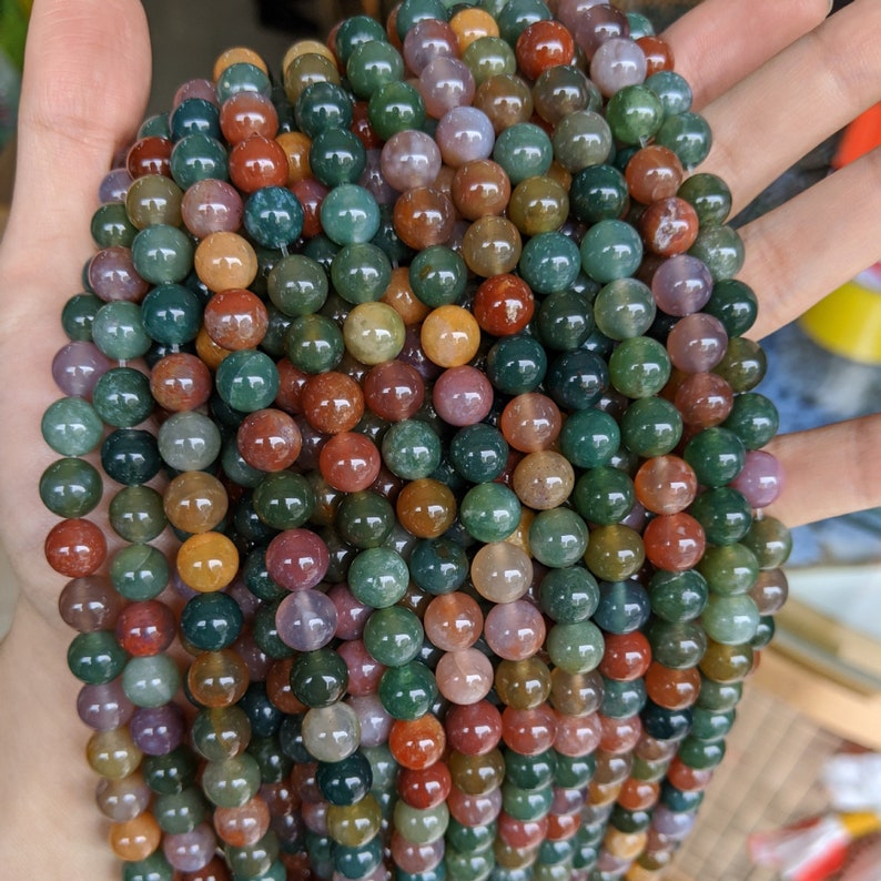 May include: A strand of multi-colored agate beads. The beads are round and have a variety of colors, including green, brown, red, and orange. The beads are strung on a clear elastic cord.