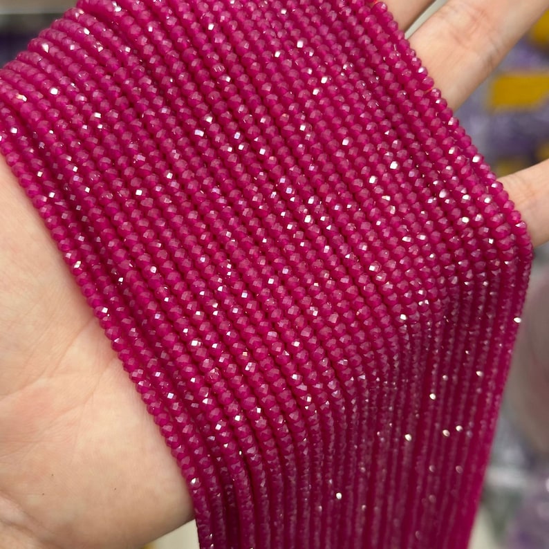 May include: A strand of pink faceted gemstone beads. The beads are small and uniform in size and shape. The strand is long and appears to be made of many individual beads.