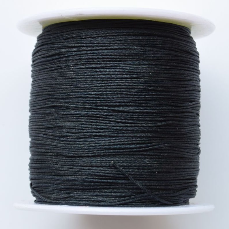 Puede incluir: Una bobina de cord&oacute;n el&aacute;stico negro, enrollada apretadamente en una bobina de pl&aacute;stico blanco.