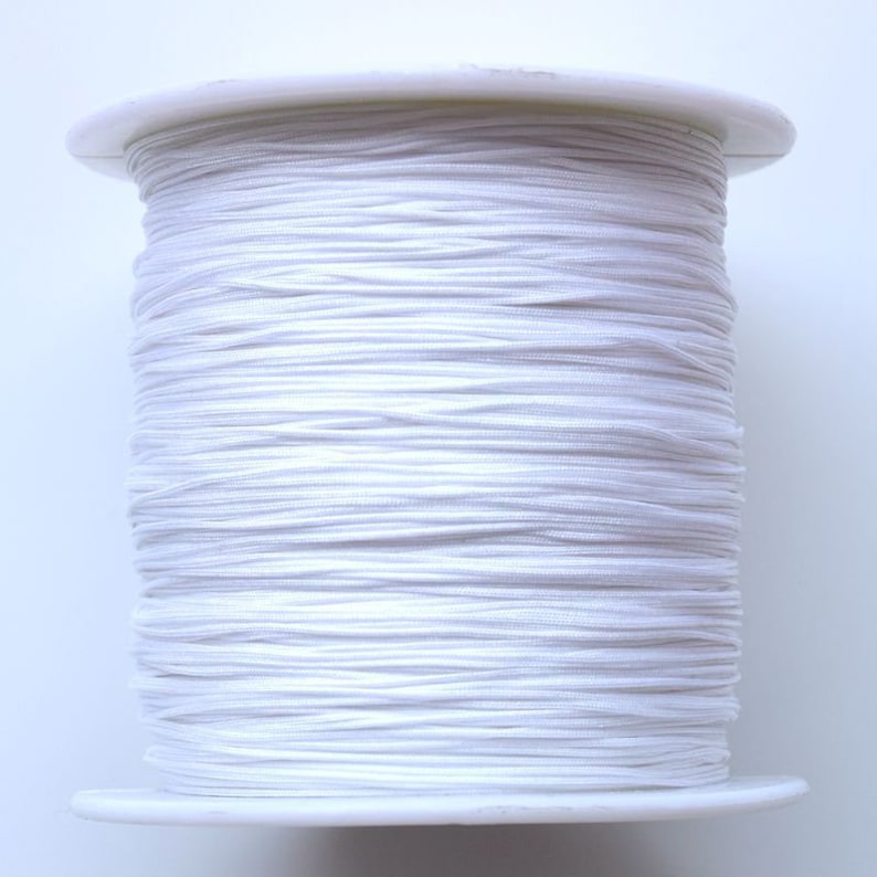 Puede incluir: Una bobina de cord&oacute;n el&aacute;stico blanco, enrollada apretadamente en una bobina de pl&aacute;stico blanca.