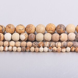 May include: A strand of brown and white jasper beads in various sizes. The beads are round and have a natural, polished finish.