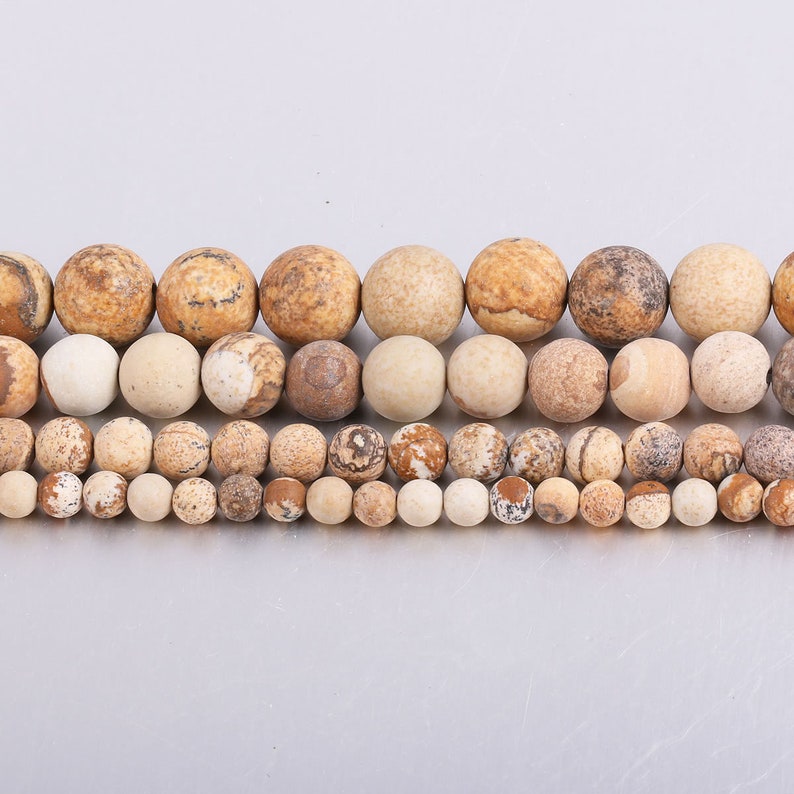 May include: A strand of brown and white jasper beads in various sizes. The beads are round and have a natural, polished finish.