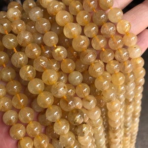 May include: A strand of round, translucent golden rutilated quartz beads. The beads are approximately 8mm in diameter and have a light yellow color with gold inclusions.