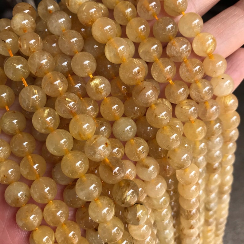 May include: A strand of round, translucent golden rutilated quartz beads. The beads are approximately 8mm in diameter and have a light yellow color with gold inclusions.