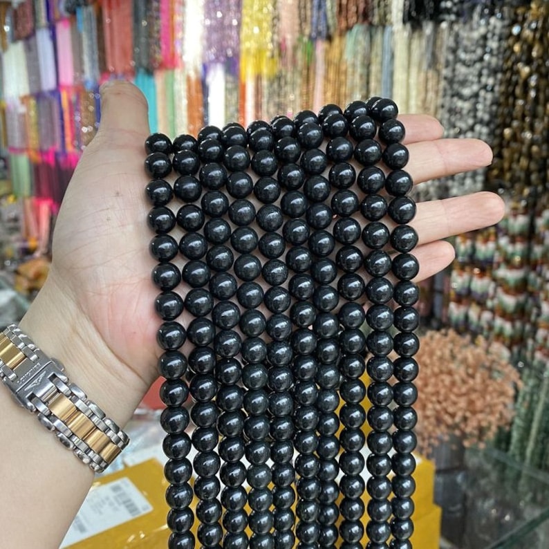 May include: A strand of black gemstone beads, possibly obsidian, strung together for jewellery making. The beads are round and smooth, with a slightly glossy finish.