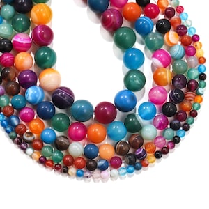 May include: A collection of colourful agate beads in various shades of blue, green, red, orange, and purple. The beads are round and have a smooth, polished finish.