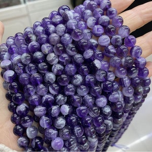 May include: A strand of round, purple amethyst beads with white swirls. The beads are smooth and polished.