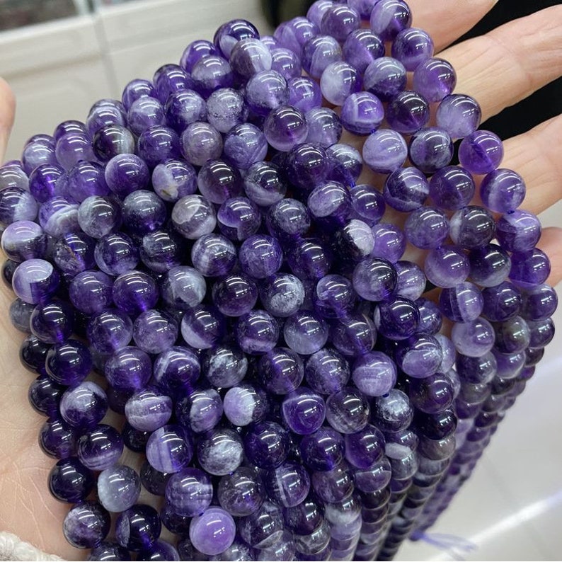 May include: A strand of round, purple amethyst beads with white swirls. The beads are smooth and polished.