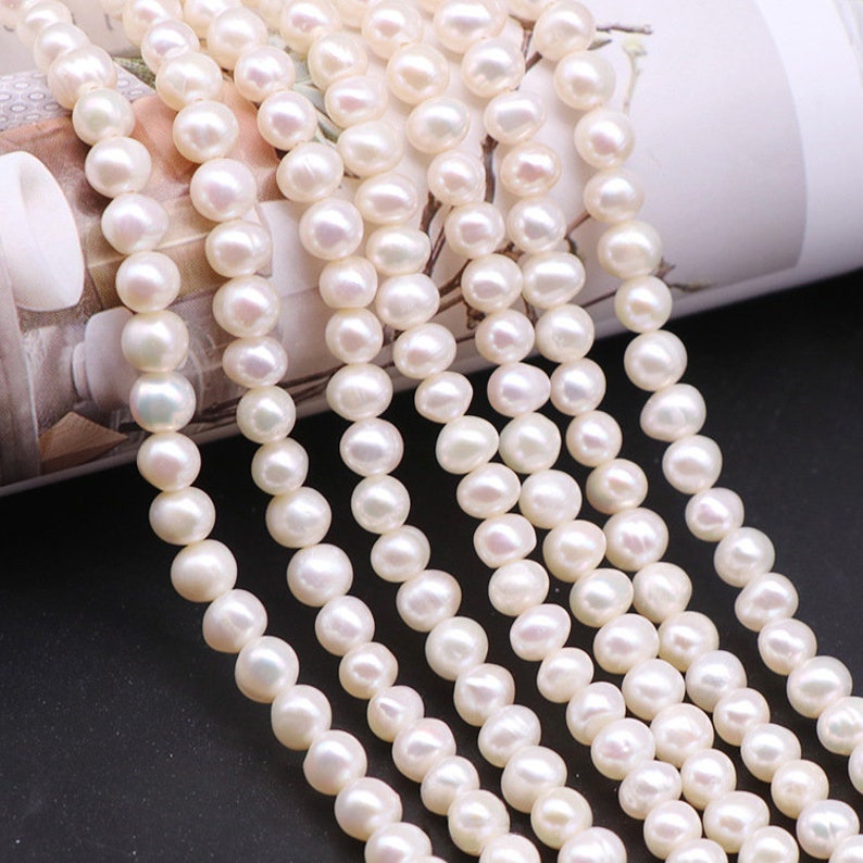 May include: A strand of white freshwater pearls, with a smooth, round shape. The pearls are strung on a clear thread and are ready to be used for jewelry making.
