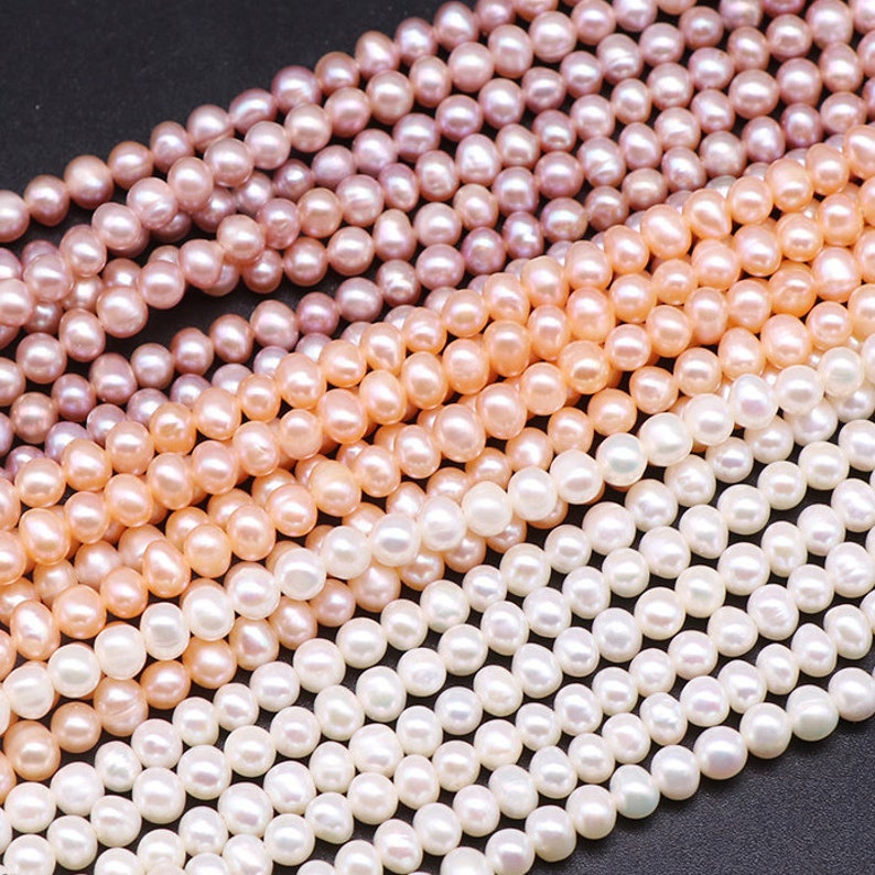 May include: A strand of white, pink, and peach freshwater pearls. The pearls are round and smooth, and they are strung on a white thread. The pearls are arranged in a graduated pattern, with the largest pearls at the top and the smallest pearls at the bottom.