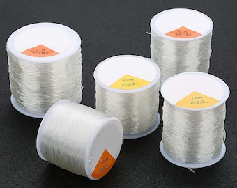 May include: Five spools of clear elastic thread, each with a white label indicating the diameter and length of the thread. The labels read "0.8 100M", "1.0 100M", "0.6 100M", "0.7 100M", and "0.5 100M".