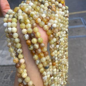 May include: A strand of yellow and white opal beads. The beads are round and have a smooth, polished finish. The strand is approximately 18 inches long.