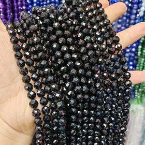 Peut inclure: Un brin de perles de pierres pr&eacute;cieuses facett&eacute;es noires. Les perles sont rondes et ont une finition brillante et iris&eacute;e.