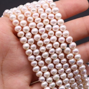 May include: A strand of white freshwater pearls, each pearl is round and smooth. The pearls are strung on a white thread and are approximately 6mm in diameter.