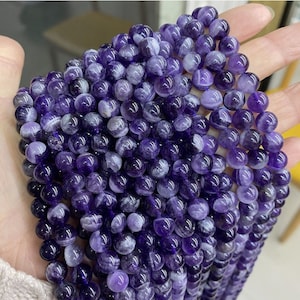 May include: A strand of round, purple amethyst beads with white swirls. The beads are smooth and polished.