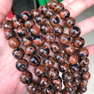May include: A strand of round, brown and black gemstone beads. The beads have a speckled, glittery appearance.