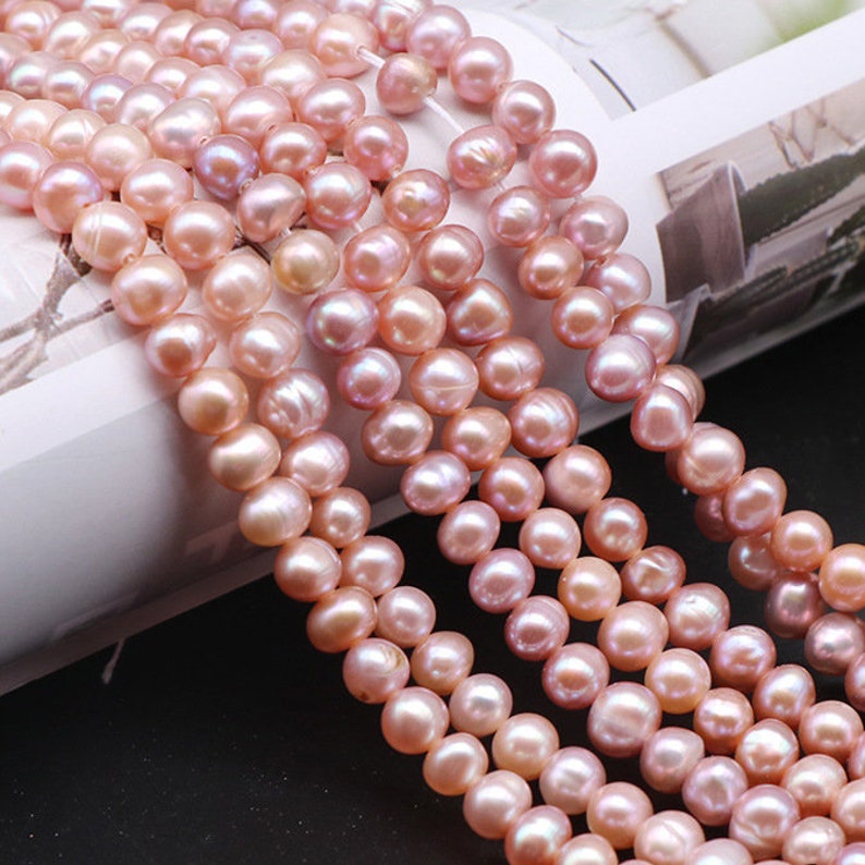 May include: A strand of pink freshwater pearls, with a slight iridescent sheen. The pearls are round and smooth, and they are strung on a clear thread.