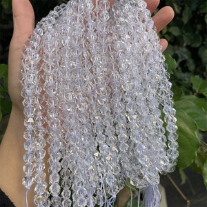 May include: A strand of clear crystal beads, each bead is faceted and has a star-like shape. The beads are strung on a white thread and are arranged in a cascading pattern.