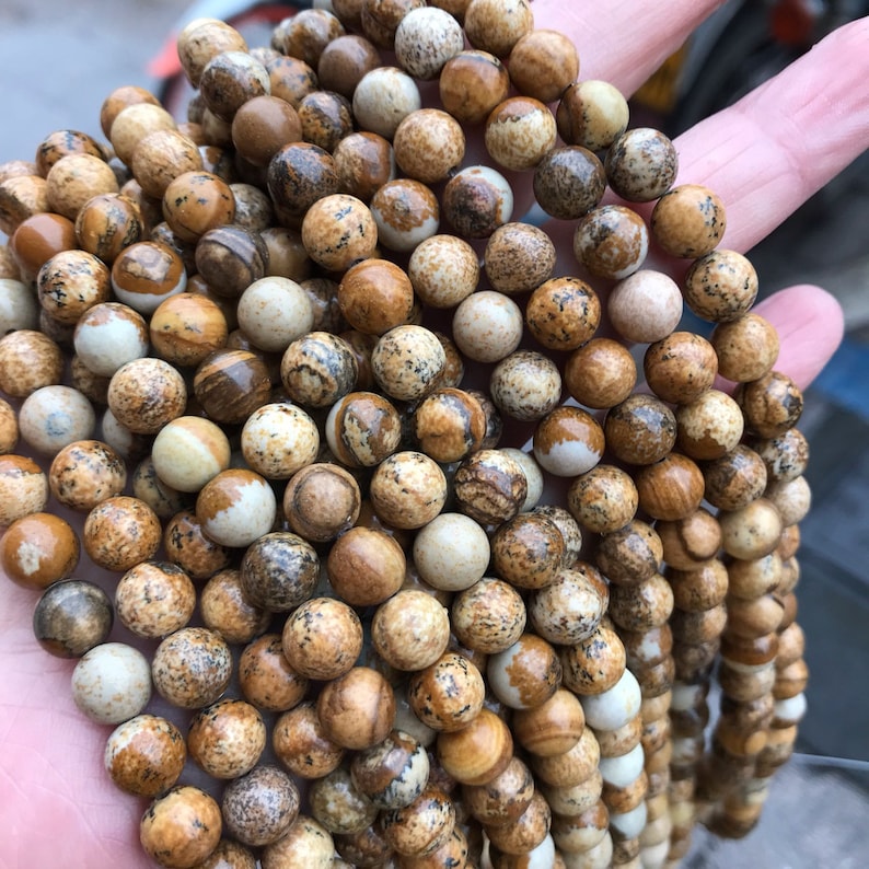 May include: A strand of brown and white jasper beads. The beads are round and have a speckled pattern.