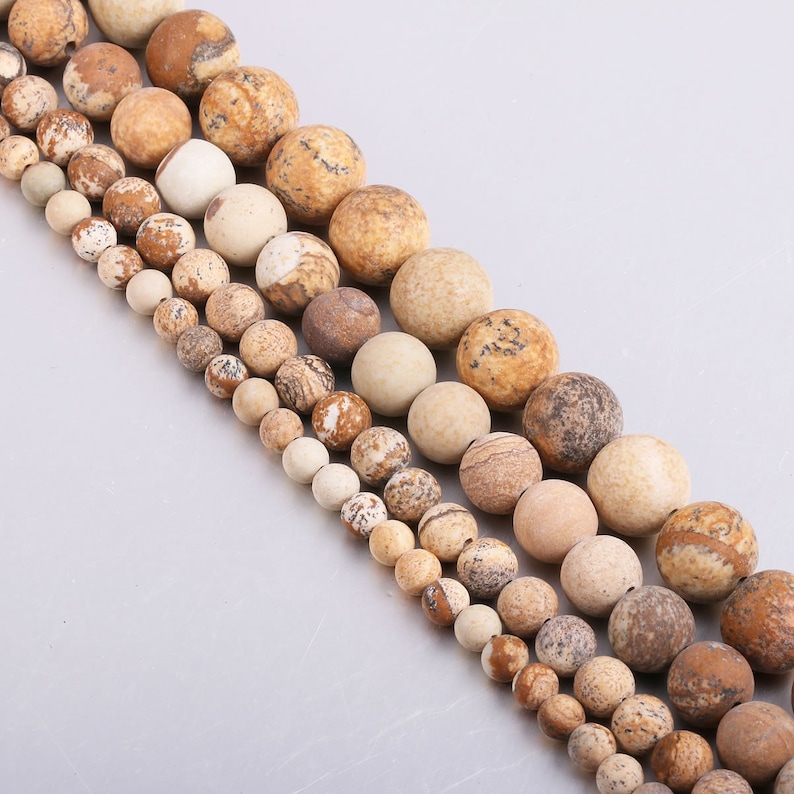 May include: A strand of brown and beige gemstone beads. The beads are round and have a natural, speckled pattern.