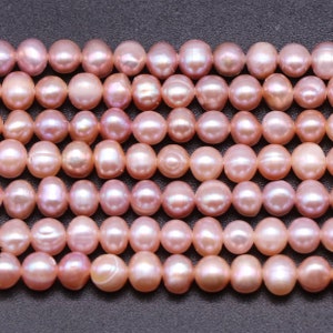 May include: A strand of pink freshwater pearls. The pearls are round and have a slight iridescent sheen.