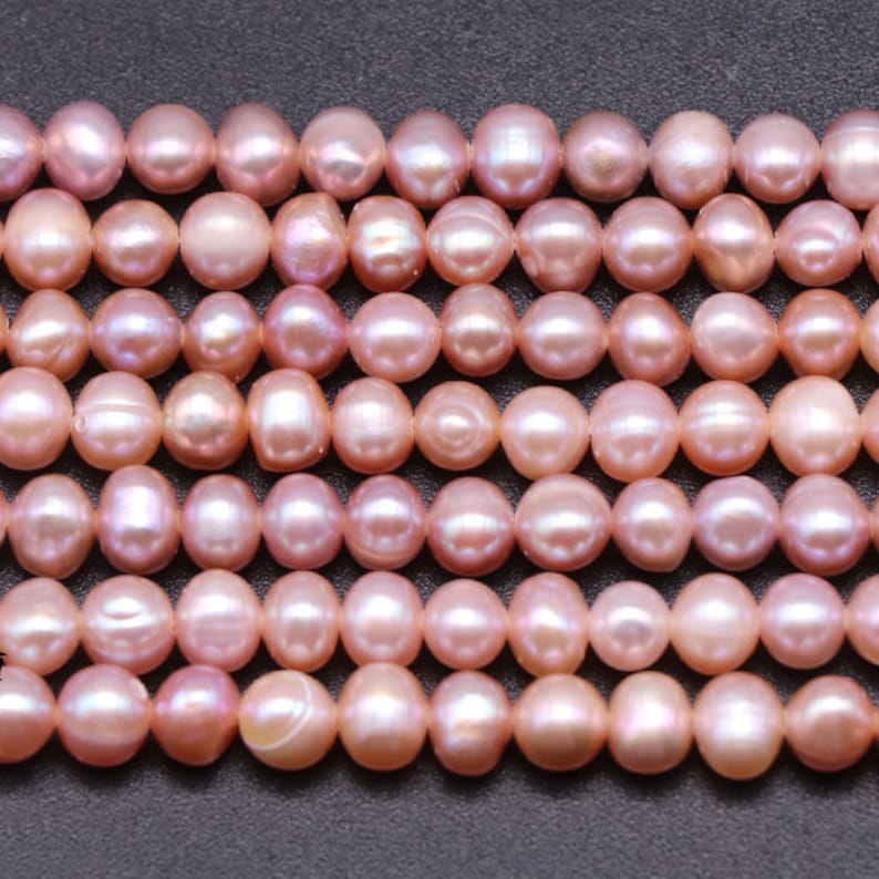 May include: A strand of pink freshwater pearls. The pearls are round and have a slight iridescent sheen.