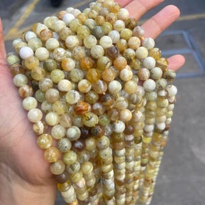 May include: A strand of round, yellow, green, and white opal beads. The beads are approximately 6mm in diameter and have a natural, irregular shape.