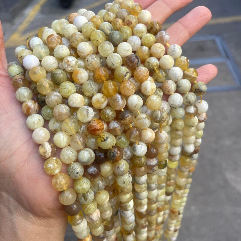 May include: A strand of round, yellow, green, and white opal beads. The beads are approximately 6mm in diameter and have a natural, irregular shape.