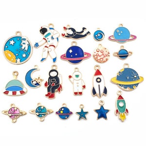 May include: A set of 18 enamel charms with a space theme. The charms feature astronauts, planets, stars, rockets, and UFOs. The charms are gold-toned and have colourful enamel details.