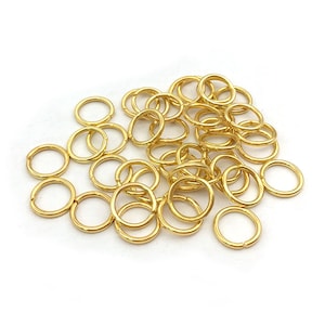 Peut inclure: Un ensemble de petits anneaux ouverts dor&eacute;s, dispos&eacute;s sur une surface blanche. Ces anneaux sont utilis&eacute;s pour la fabrication de bijoux et l'artisanat. Les anneaux sont en m&eacute;tal et ont une finition brillante.