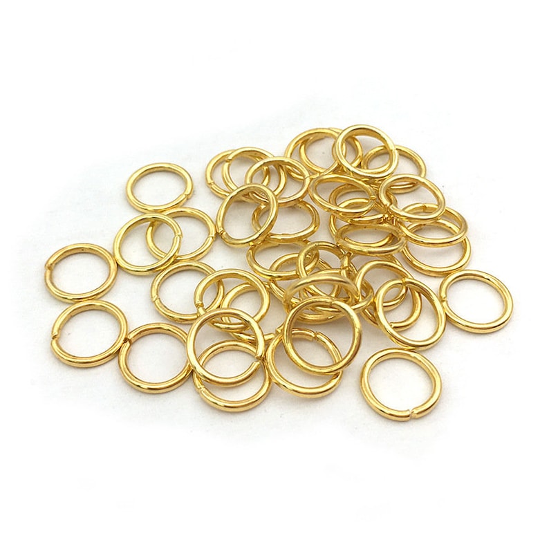 Peut inclure: Un ensemble de petits anneaux ouverts dor&eacute;s, dispos&eacute;s sur une surface blanche. Ces anneaux sont utilis&eacute;s pour la fabrication de bijoux et l'artisanat. Les anneaux sont en m&eacute;tal et ont une finition brillante.