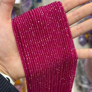 May include: A strand of faceted ruby red gemstone beads. The beads are small and uniform in size and shape. The strand is long and appears to be made of many individual beads.