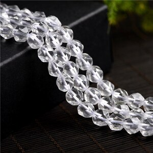 May include: A strand of clear faceted crystal beads. The beads are strung on a white thread and are arranged in a staggered pattern. The beads are all the same size and shape.
