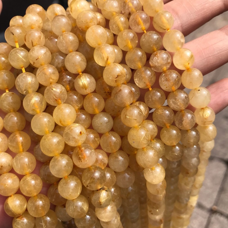May include: A strand of golden rutilated quartz beads. The beads are round and translucent, with gold inclusions that sparkle in the light.