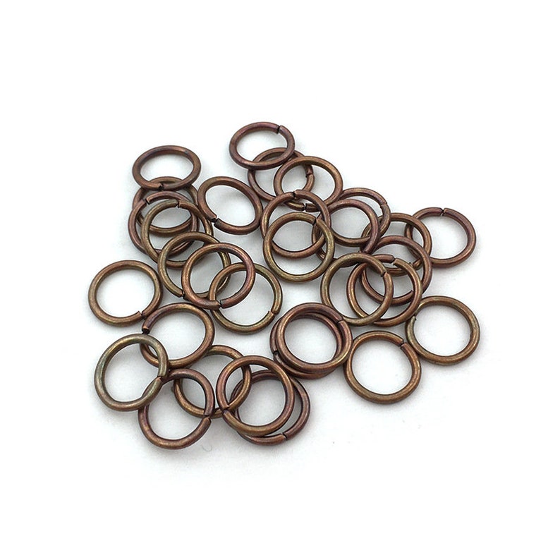 Peut inclure: Un ensemble de petits anneaux ouverts de couleur bronze, dispers&eacute;s sur une surface blanche. Les anneaux sont circulaires et semblent &ecirc;tre en m&eacute;tal, adapt&eacute;s &agrave; la fabrication de bijoux ou &agrave; l'artisanat.