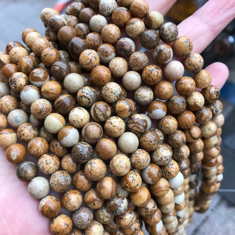 May include: A strand of brown and white jasper beads. The beads are round and have a speckled pattern.