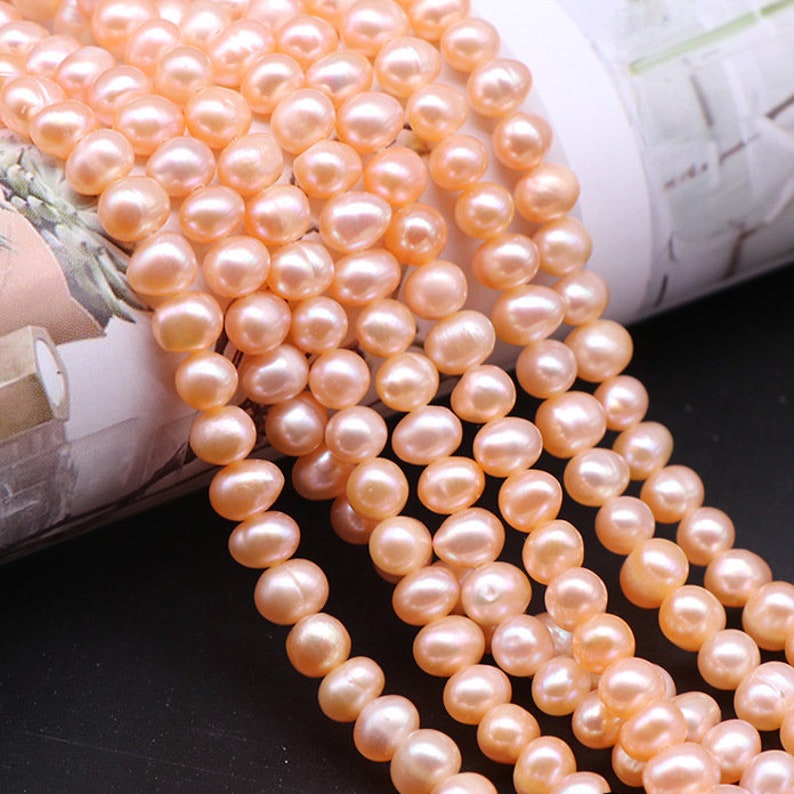May include: A strand of pale pink freshwater pearls. The pearls are round and smooth, and they are strung on a white thread. The pearls are arranged in a row, and they are all the same size.