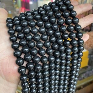 May include: A strand of black obsidian beads, each bead is round and smooth. The beads are strung together on a clear thread.