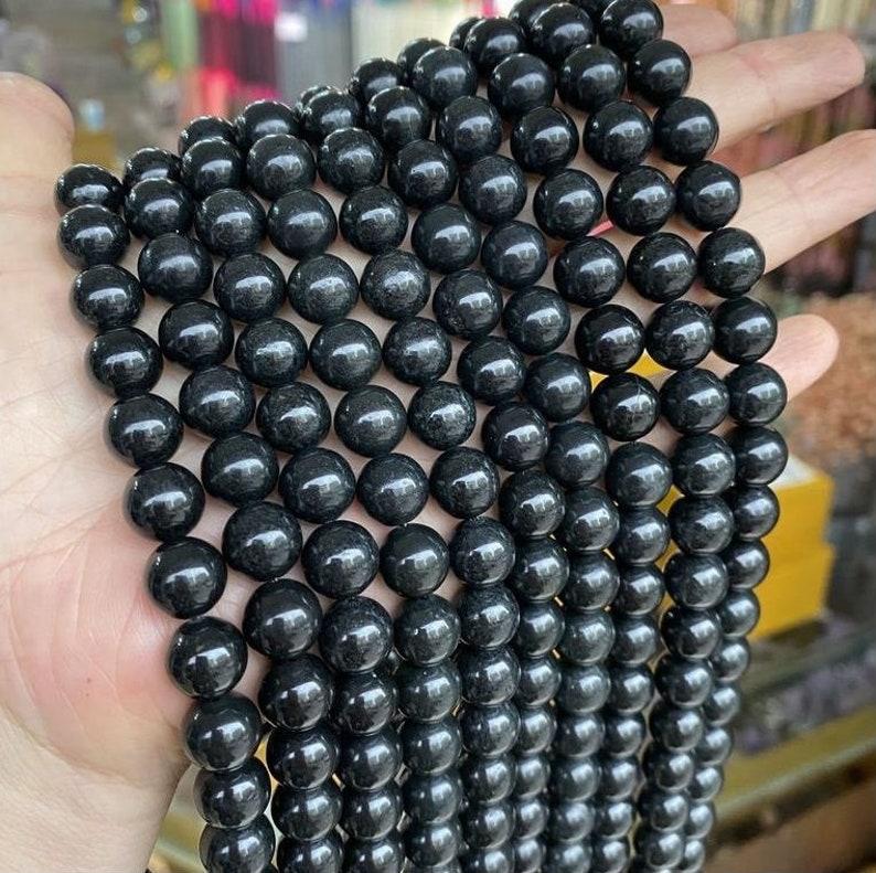 May include: A strand of black obsidian beads, each bead is round and smooth. The beads are strung together on a clear thread.