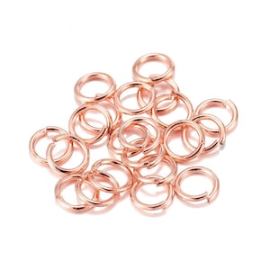 Peut inclure: Un ensemble de anneaux de saut en or rose, dispers&eacute;s sur une surface blanche. Les anneaux sont ouverts, pr&ecirc;ts &agrave; &ecirc;tre utilis&eacute;s dans la fabrication de bijoux ou d'autres travaux manuels. Le m&eacute;tal a une finition brillante.