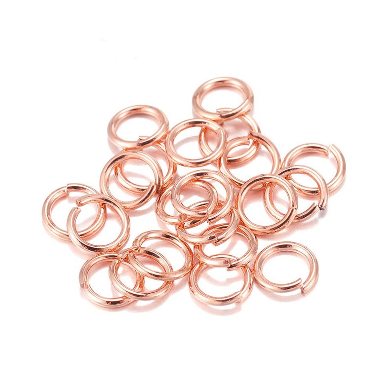 Peut inclure: Un ensemble de anneaux de saut en or rose, dispers&eacute;s sur une surface blanche. Les anneaux sont ouverts, pr&ecirc;ts &agrave; &ecirc;tre utilis&eacute;s dans la fabrication de bijoux ou d'autres travaux manuels. Le m&eacute;tal a une finition brillante.