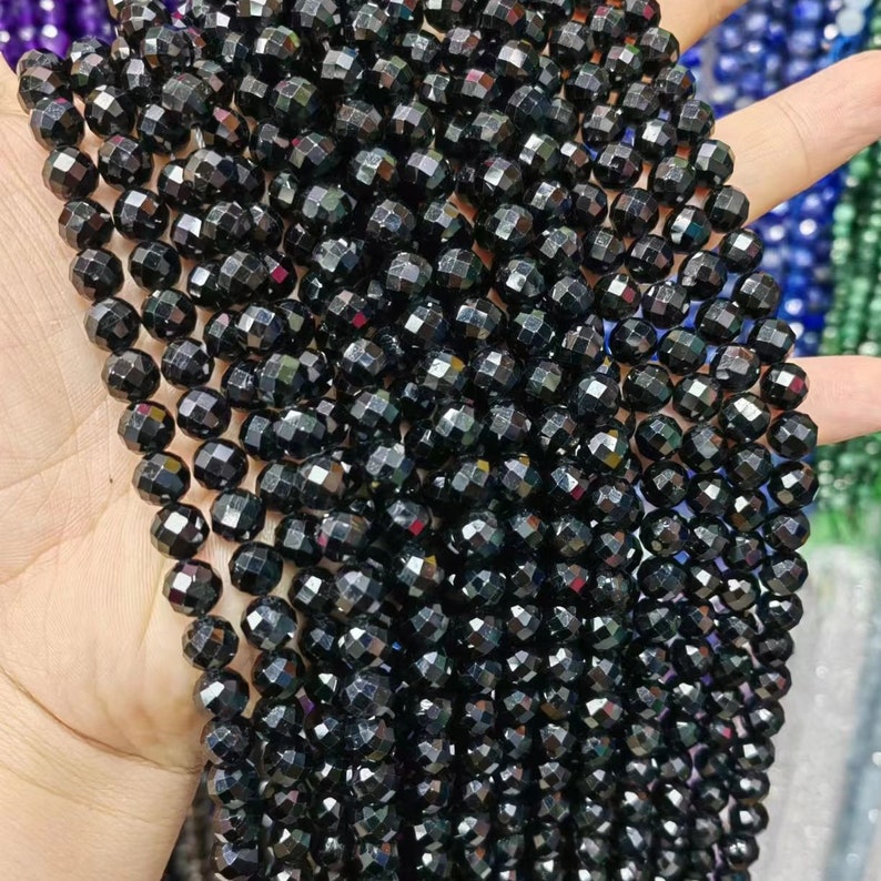 Peut inclure: Un brin de perles de pierres pr&eacute;cieuses facett&eacute;es noires. Les perles sont rondes et ont une finition brillante et iris&eacute;e.