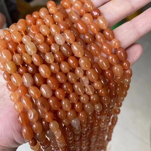 Puede incluir: Una hebra de cuentas de cornalina naranja, cada cuenta es de forma ovalada y pulida. Las cuentas est&aacute;n enhebradas en un hilo transparente.