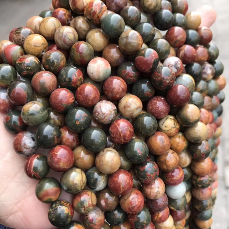 May include: A strand of round, multi-colored gemstone beads. The beads are a mix of brown, red, green, and white. The beads are all about 10mm in diameter.