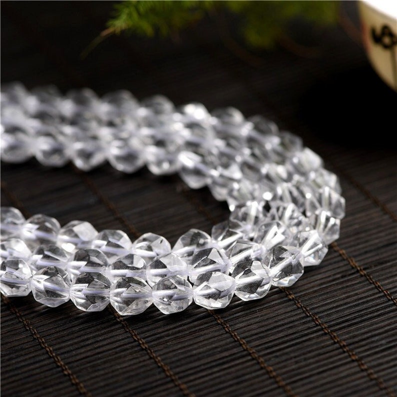 May include: A strand of clear faceted crystal beads. The beads are strung on a white thread and are arranged in a circular pattern.