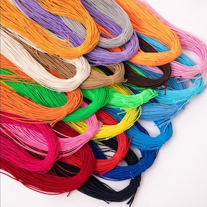 Könnte beinhalten: Eine Sammlung mehrerer Bündel aus dünner, elastischer Kordel in einer Vielzahl lebendiger Farben, darunter Orange, Lila, Grau, Weiß, Braun, Grün, Gelb, Pink, Rot, Dunkelblau und Hellblau, die jeweils zu einer Schlaufe gebunden sind.