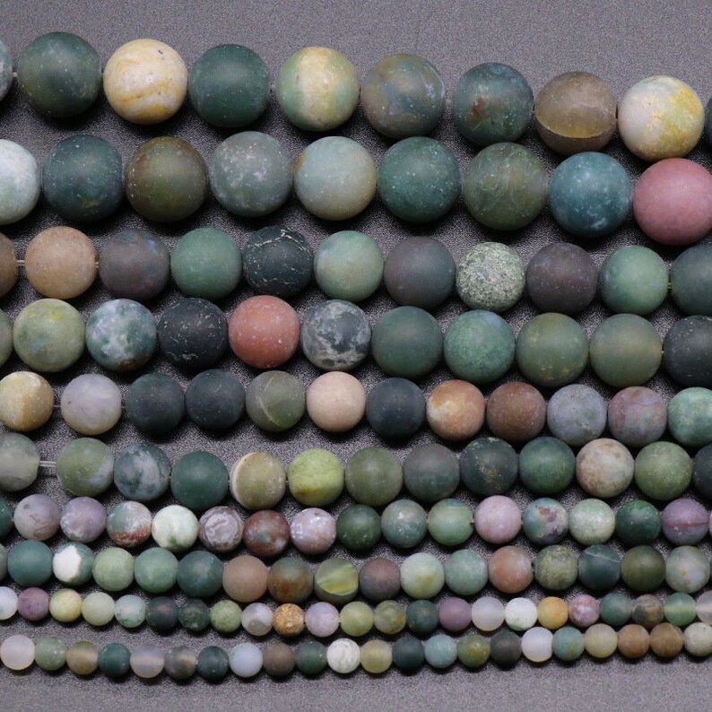 May include: A collection of round, green, brown, and white agate beads. The beads are various sizes and have a mottled, natural appearance.