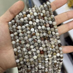 May include: A handful of round, natural stone beads in shades of gray, brown, and white. The beads have a marbled appearance and are strung together, suggesting they are for jewelry making or crafts.