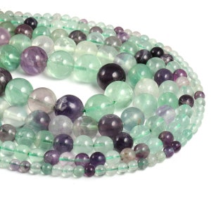 May include: A strand of round, green and purple fluorite beads. The beads are smooth and polished, and they have a natural, translucent appearance.