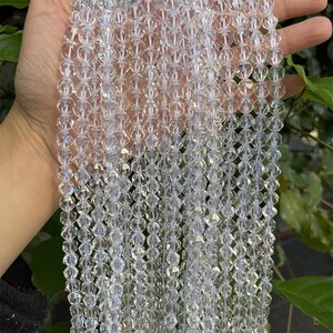May include: A strand of clear faceted crystal beads. The beads are small and round, and they are strung on a clear thread. The beads are arranged in a straight line, and they are all the same size and shape.